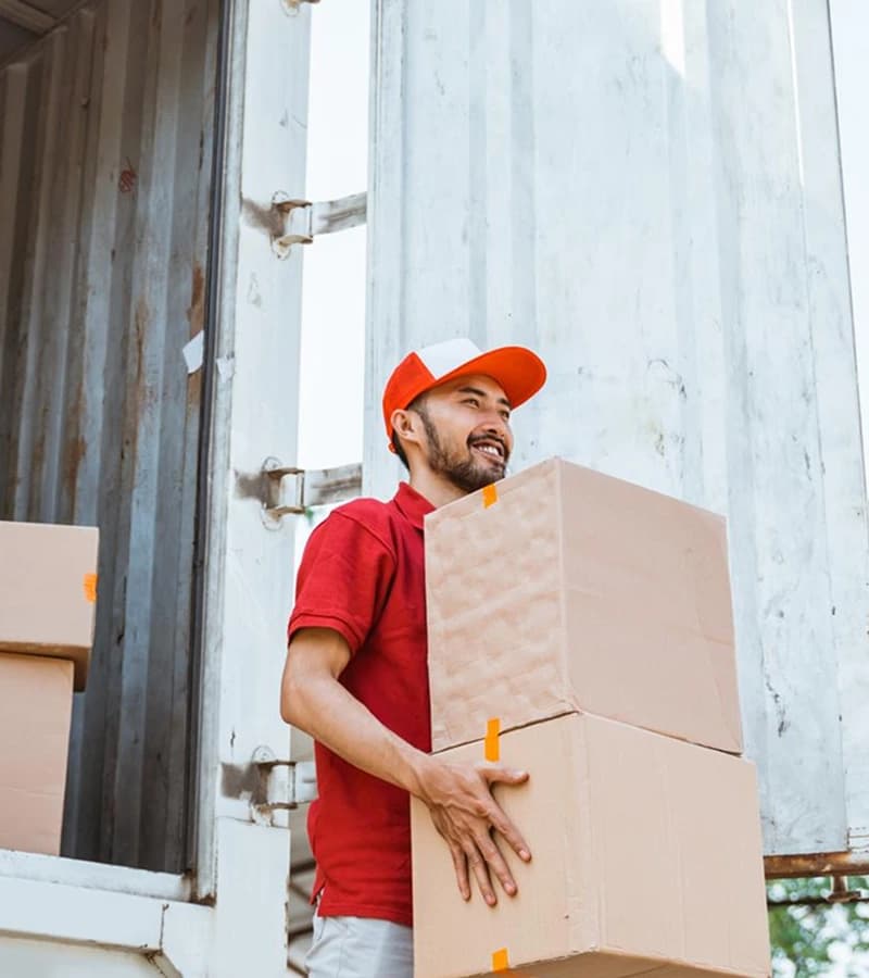 Delivery worker in red uniform carrying a cardboard box for expedited and hot shot freight services